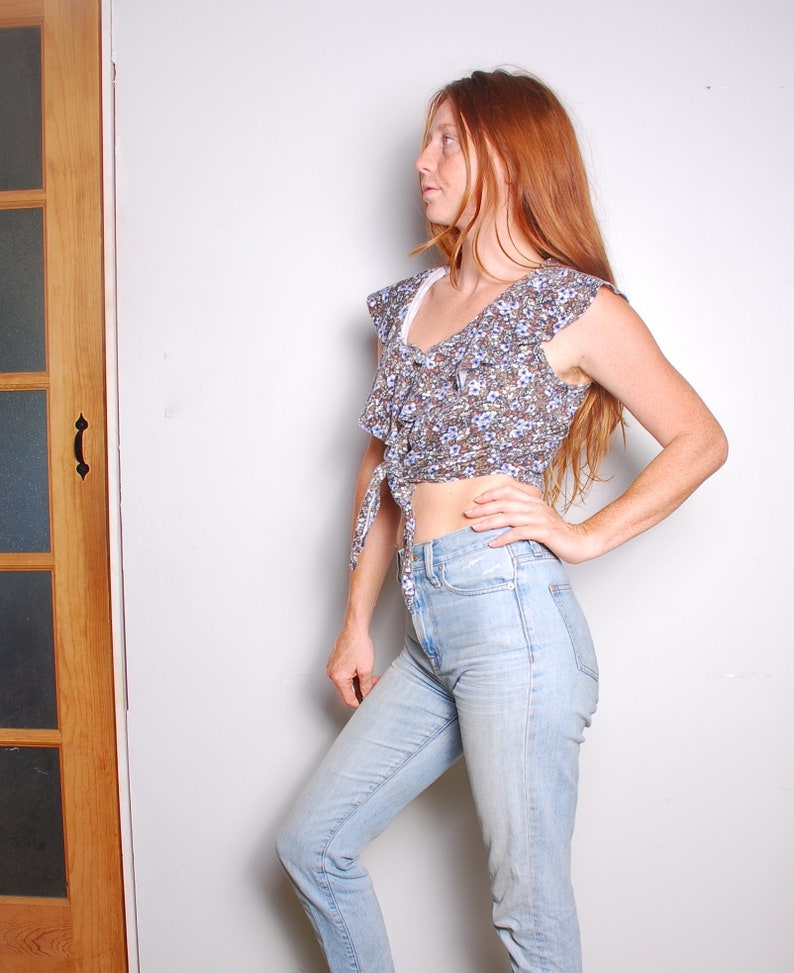 May include: A woman wearing a blue and white floral print crop top with a ruffled neckline and light blue jeans.