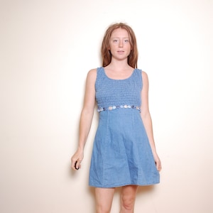 May include: A woman wearing a light blue denim dress with a floral trim around the waist.