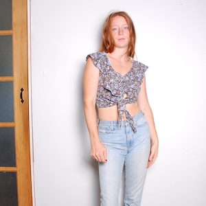 May include: A woman wearing a floral print crop top with a tie front and light blue jeans.
