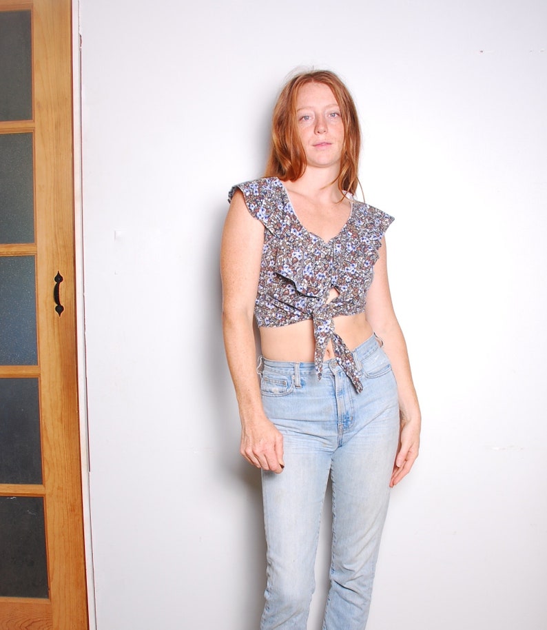 May include: A woman wearing a floral print crop top with a tie front and light blue jeans.