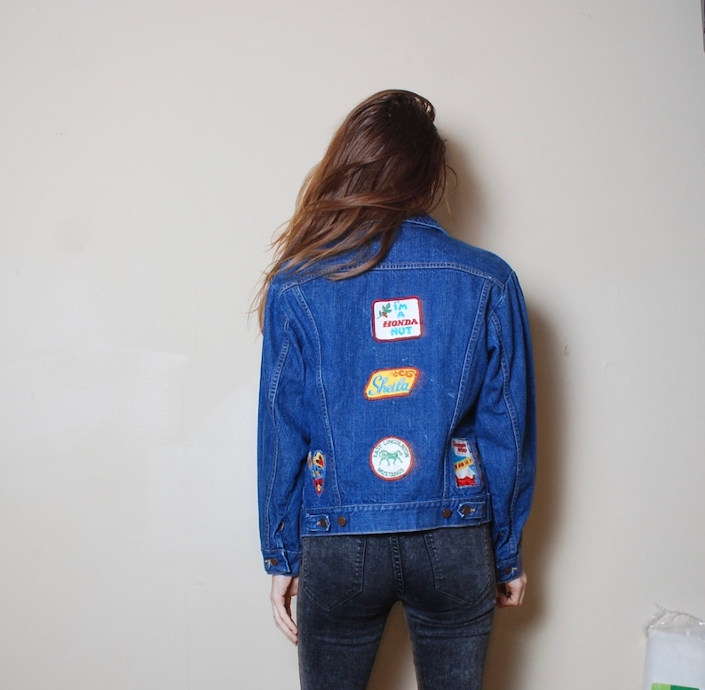 Puede incluir: Una chaqueta vaquera azul con varios parches bordados, incluyendo "I'm a Honda Nut", "Sheena" y un tr&eacute;bol verde.