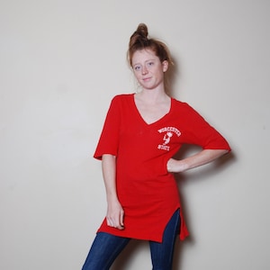 May include: A red long-sleeved t-shirt with a side slit. The shirt has a white graphic of a person with the text "Worcester State" on the front.