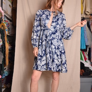 May include: A blue and white floral print mini dress with long sleeves and a keyhole neckline. The dress has a gathered skirt and a relaxed fit.