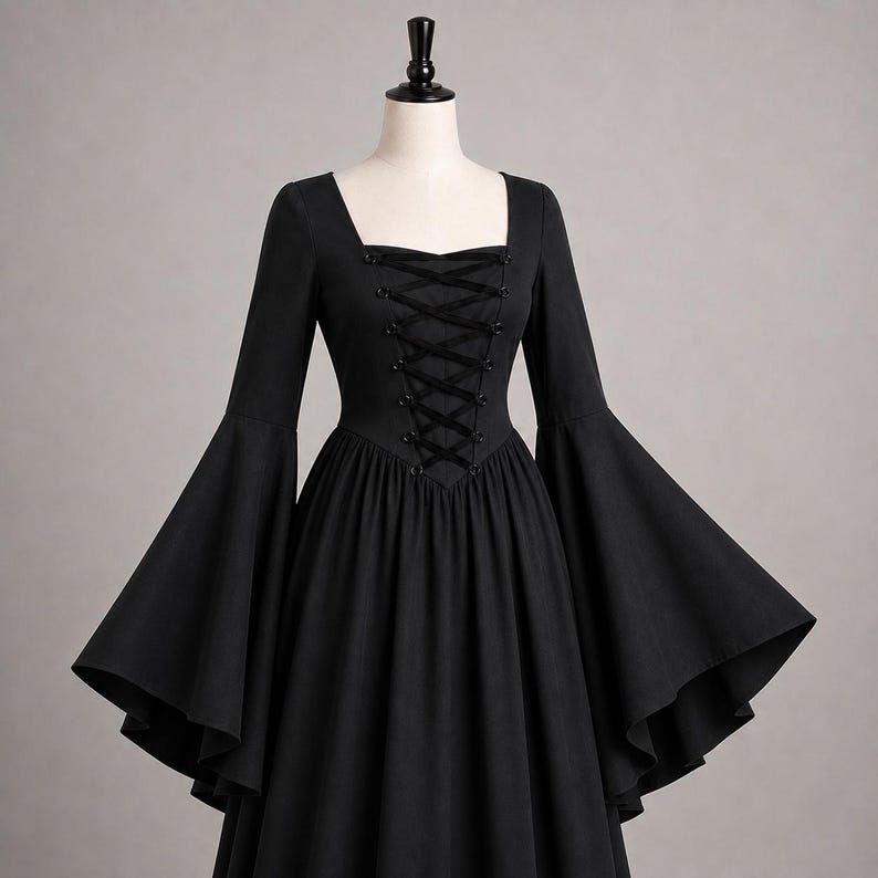 May include: A solid black dress featuring a square neckline, long flared bell sleeves, and a central bodice panel with black ribbon lace-up detailing. The garment has a fitted waistline that transitions into a full, flowing skirt silhouette.