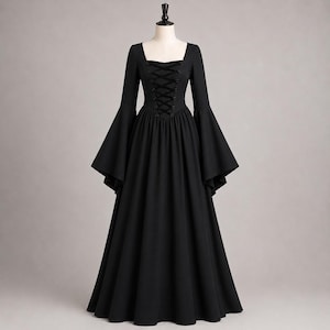 May include: A floor-length black dress featuring long flared sleeves, a square neckline, and a central bodice panel with a black lace-up corset-style closure. The garment has a fitted waist that transitions into a full, flowing skirt.