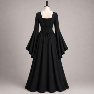 May include: A floor-length black dress featuring long, wide bell sleeves and a square neckline. The back of the bodice includes a corset-style lace-up closure with matching black laces, creating a fitted silhouette that flows into a full skirt.