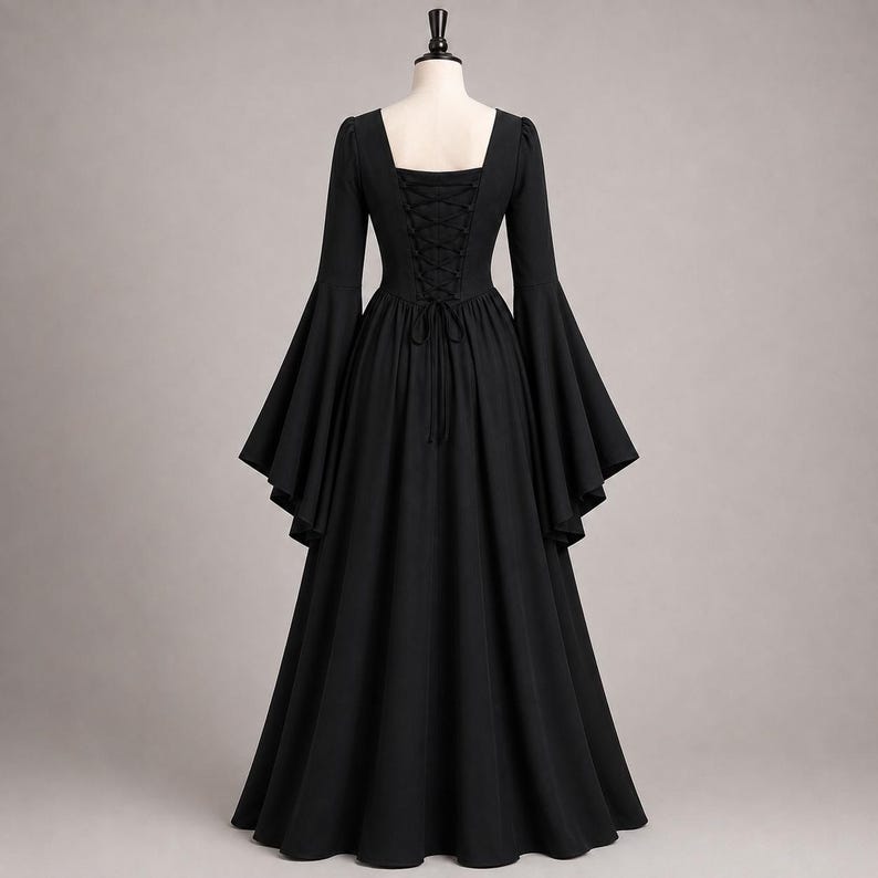 May include: A floor-length black dress featuring long, wide bell sleeves and a square neckline. The back of the bodice includes a corset-style lace-up closure with matching black laces, creating a fitted silhouette that flows into a full skirt.