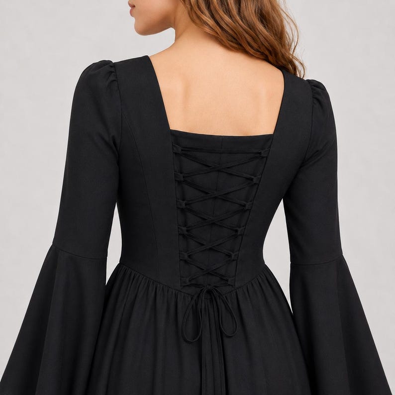 May include: A black long-sleeved dress featuring a square neckline and flared bell sleeves. The back of the bodice includes a corset-style lace-up closure with matching black fabric ties that are knotted at the waist, creating a fitted silhouette.