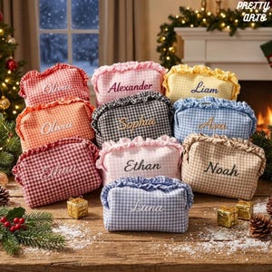 Puede incluir: Una colección de estuches rectangulares de tela con estampado de cuadros vichy en varios colores, incluyendo rojo, naranja, rosa, negro, amarillo, azul y beige. Cada estuche tiene un borde superior con volantes y un nombre bordado.