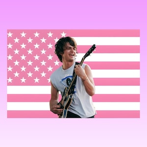 Op de afbeelding: Een persoon met donker haar draagt een wit mouwloos shirt en bespeelt een zwarte elektrische gitaar. De achtergrond toont een gestileerde Amerikaanse vlag met horizontale strepen en sterren in roze en witte tinten voor een levendig contrast.