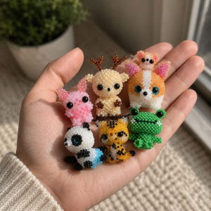 Könnte beinhalten: Eine Sammlung von sieben Miniatur-Tierfiguren aus kleinen Perlen. Das Set enthält einen rosa Hasen, ein beiges Reh mit braunem Geweih, einen weiß-orangen Corgi, einen grünen Frosch, einen schwarz-weißen Panda und einen gelben Tiger.