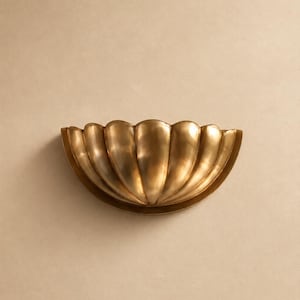May include: A semi-circular wall sconce featuring a metallic gold finish and a scalloped, shell-like design with vertical ridges. The fixture has a curved, bowl-shaped structure that projects outward, creating a symmetrical, fan-like appearance.