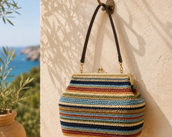 May include: A crochet handbag featuring horizontal stripes in shades of navy blue, light blue, cream, olive green, and rust red. The bag has a brass-toned metal frame with a kiss-lock closure and a single dark brown leather handle attached to the frame.