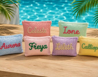 May include: Six rectangular zippered pouches made of textured fabric in various pastel colors. Each pouch features a name embroidered in a contrasting color: Aurora in pink, Celeste in cream, Freya in green, Ione in pink, Lilith in cream, and Calliopa in green.