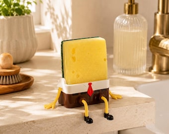 May include: A yellow rectangular sponge held by a brown plastic base with white trim, a red tie, and yellow legs with black shoes. The base features a small shelf design that supports the sponge upright, creating a character-like appearance.