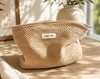 May include: A beige woven pouch with a herringbone pattern and a zipper closure. A small white rectangular fabric label is sewn onto the front, featuring the black printed text "simple wish" in a lowercase sans-serif font.