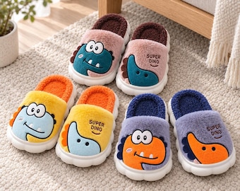 May include: Three pairs of plush slippers with thick white soles. Each pair features a different color scheme: pink and dark brown, yellow and orange, and light purple and dark blue. Each slipper displays a cartoon dinosaur face and the text SUPER DINO.