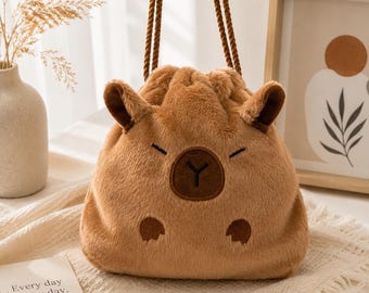 May include: A brown plush drawstring bag shaped like a capybara, featuring embroidered facial details, two small ears, and two front paws. The bag has two brown twisted rope handles and a soft, fuzzy texture throughout the exterior surface.