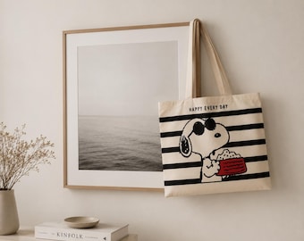May include: A cream-colored canvas tote bag featuring horizontal black stripes and a graphic of a white cartoon dog wearing black sunglasses and holding a red rectangular object. The text "HAPPY EVERY DAY" is printed in black above the dog.