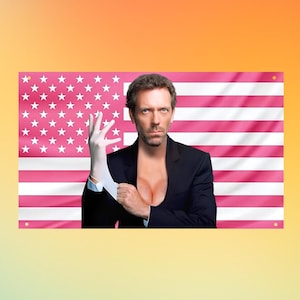 以下が含まれることがあります： ピンクと白の色合いで水平のアメリカ国旗パターンを特徴とする長方形の壁掛け旗。旗の中央には、短い茶色の髪でダークブレザーを着た男性の肖像画があり、片手に白い医療用手袋をはめている様子が描かれています。