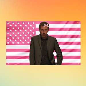 Könnte beinhalten: Ein rechteckiges Wandbanner mit einem rosa-weißen amerikanischen Flaggenmuster. In der Mitte der Flagge befindet sich das Porträt einer Person mit kurzem braunem Haar, die einen dunkelbraunen Blazer über einem schwarzen Hemd und eine kleine hellrosa Schleife auf dem Kopf trägt.