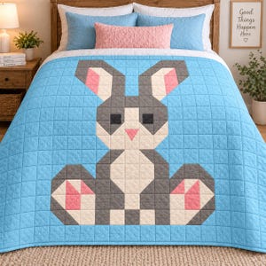 Puede incluir: Una colcha de color azul claro con un diseño grande y centrado de un conejo pixelado. El conejo está construido con cuadrados de tela gris, blanca y rosa. La colcha tiene un patrón de costuras en cuadrícula que crea una apariencia texturizada.