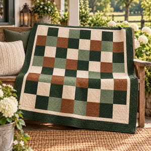 May include: A square quilt featuring a checkered pattern of alternating dark green, sage green, cream, and terracotta brown fabric squares. The quilt is finished with a solid dark green border and displays a visible quilted texture throughout the fabric.
