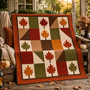 May include: A square quilt featuring a grid pattern of alternating blocks. Some blocks display appliqued maple leaves in shades of red, orange, and green, while others are solid squares or triangles in brown, tan, and cream colors with a border.