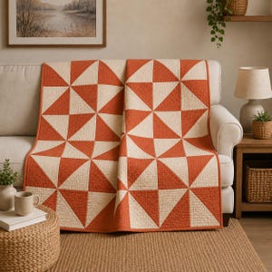 May include: A quilt featuring a geometric pattern of alternating burnt orange and cream-colored triangles. The fabric has a visible quilted texture throughout, and the entire piece is finished with a solid burnt orange fabric border trim.
