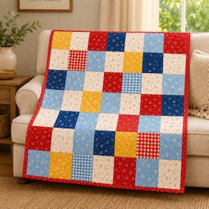 Könnte beinhalten: Eine Patchwork-Decke mit einem Raster aus quadratischen Stoffblöcken in Rot, Blau, Gelb und Creme. Das Muster umfasst florale Drucke, Vichy-Karos und einfarbige Stoffe, die mit einem roten Rand und einer sichtbaren Steppstruktur vernäht sind.
