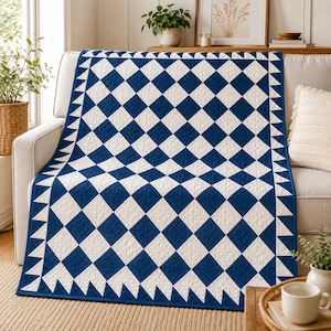 Puede incluir: Una colcha rectangular con un patrón repetitivo de diamantes en azul marino intenso y blanco roto. La colcha está rematada con un borde de triángulos alternos en azul marino y blanco a lo largo de los cuatro lados, creando un diseño geométrico.