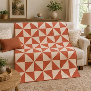 May include: A rectangular quilt featuring a repeating geometric pattern of terracotta orange and cream-coloured triangles. The fabric has a visible quilted texture throughout, creating a grid of squares composed of two contrasting triangular halves.