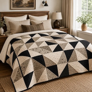 May include: A quilt featuring a geometric pattern of triangles in black, cream, and mottled brown tones. The bedspread has a quilted texture and covers a bed with two large cream pillows, two tan pillows, and one small rectangular brown striped pillow.