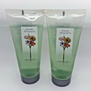 Pode incluir: Dois tubos de plástico transparente de gel de banho e duche Avon Floral Prints Fresh Flowers. Cada tubo contém um líquido verde claro e apresenta um rótulo com uma ilustração floral, o texto fresh flowers e 200 ml de volume.