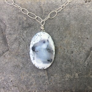 May include: A silver chain necklace with a large oval pendant made of white and black dendritic agate.