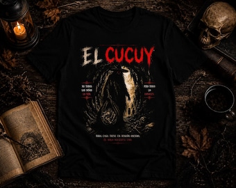 May include: A black t-shirt featuring a graphic print of a dark, hooded figure standing in a cave entrance. The text reads EL CUCUY, NO TODOS LOS NIÑOS LO VEN, PERO TODOS LO CONOCEN, and TODA CASA TIENE UN RINCÓN OSCURO. EL SOLO NECESITA UNO.