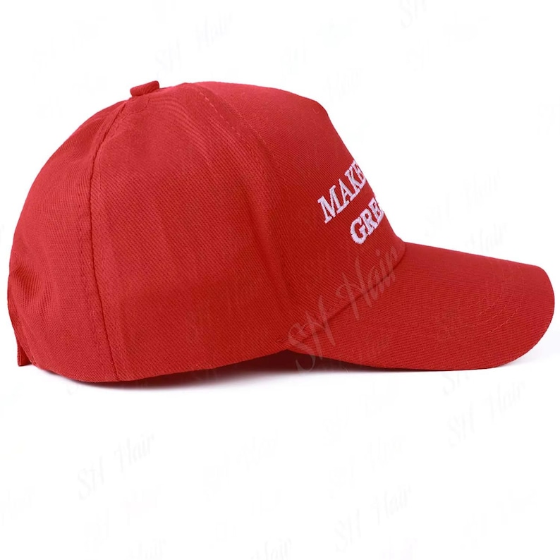 May include: A bright red baseball cap featuring white embroidered text on the side that reads MAKE GREAT. The cap has a structured crown, a curved brim, and a button at the top center, presented from a side profile view against a plain background.