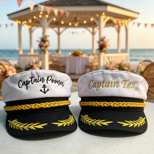 May include: Two white and black captain hats with gold braided trim and yellow embroidered laurel leaves on the brim. The left hat features the black embroidered text Captain Pooner with an anchor, and the right hat features gold embroidered text Captain Tex.
