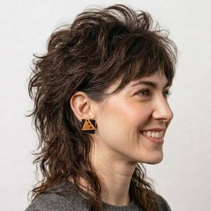May include: A square-shaped earring featuring a black base with a mustard yellow triangular accent. The earring has a flat, geometric design with three small circular cutouts arranged in a line along the yellow triangle portion.