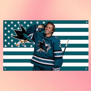 May include: A rectangular wall banner featuring a teal and white striped background with a field of white stars. A hockey player in a teal jersey with a shark logo and black and white stripes holds a hockey stick against the flag-inspired backdrop.