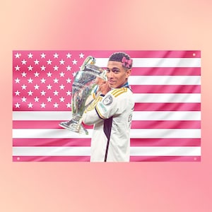 Könnte beinhalten: Eine rechteckige Wandflagge mit einem rosa-weißen amerikanischen Flaggenmuster. Eine Person in einem weißen Sporttrikot hält einen großen silbernen Pokal. Die Person trägt eine kleine rosa Schleifengrafik im Haar vor dem Flaggenhintergrund.