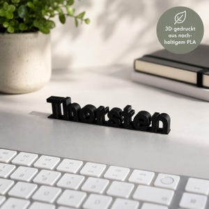 K&ouml;nnte beinhalten: Ein schwarzes, 3D-gedrucktes Namensschild mit dem Namen Thorsten in einer fetten, serifenlosen Schrift. Die Buchstaben sind an der Basis miteinander verbunden und bilden ein stabiles Objekt, das auf einer ebenen Fl&auml;che stehen kann.