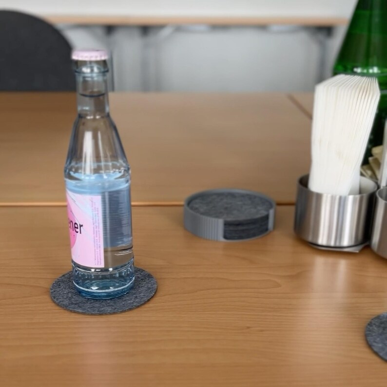 Runder Untersetzerhalter in Grau mit Stone-Grey-Filzuntersetzern auf einem Holztisch, eine Wasserflasche steht auf einem der Untersetzer (Untersetzer nicht im Lieferumfang)