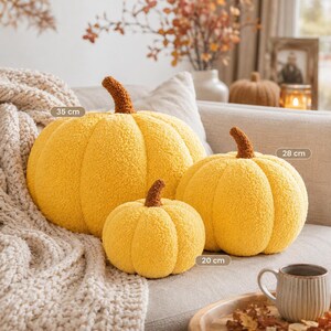 May include: Three yellow pumpkin-shaped pillows with brown stems, featuring a textured, fuzzy fabric. The pillows are labeled with sizes of 35 cm, 28 cm, and 20 cm. These decorative items have a rounded, segmented design and a soft, plush appearance.