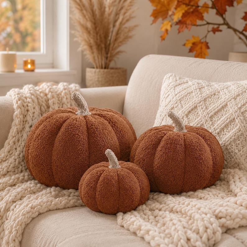May include: Three round, rust-colored pumpkin-shaped pillows made of textured, fuzzy fabric. Each pillow features a short, light-colored stem at the top. The pillows vary in size and are arranged together, showcasing a soft, plush, and rounded appearance.