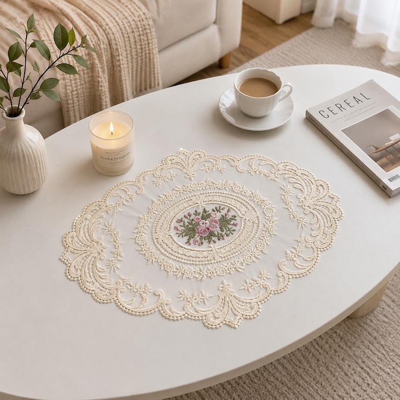 May include: An oval-shaped cream-colored lace doily featuring an intricate embroidered floral center with pink roses and green leaves, surrounded by a detailed scalloped border with elaborate openwork patterns and decorative stitching.