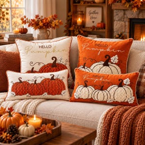 Könnte beinhalten: Vier dekorative Kissen mit gestickten Kürbissen und dem Text Hello Pumpkin. Zwei Kissen sind cremefarben mit orangefarbenen Kürbissen und zwei sind orange mit weißen Kürbissen, alle mit strukturierten Kürbismotiven versehen.
