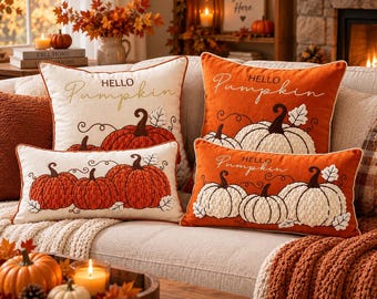May include: Four decorative throw pillows featuring embroidered pumpkins and the text Hello Pumpkin. Two pillows are cream-colored with orange pumpkins, and two are orange-colored with white pumpkins, all showcasing textured pumpkin designs.