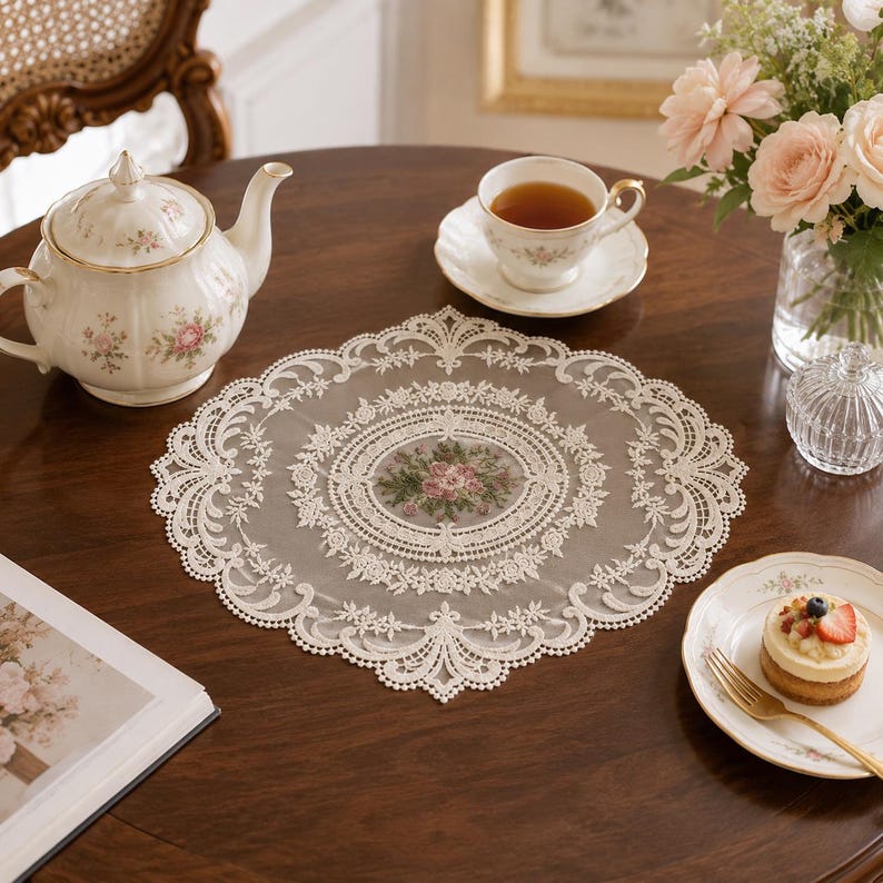 May include: A round, cream-colored lace doily featuring an intricate floral embroidery pattern in the center, surrounded by detailed scalloped lace borders. The delicate fabric is semi-sheer, showcasing a complex, symmetrical design of leaves and petals.