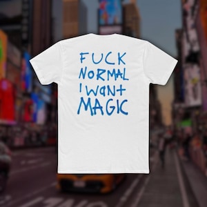 Puede incluir: Una camiseta blanca de manga corta con texto azul impreso en la parte posterior. El texto dice FUCK NORMAL I WANT MAGIC en una fuente de estilo graffiti escrito a mano. La camiseta tiene cuello redondo y corte estándar, vista trasera.